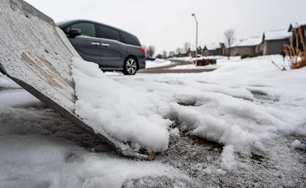 Snow removal manually with a long handled shovel on concrete driveway.